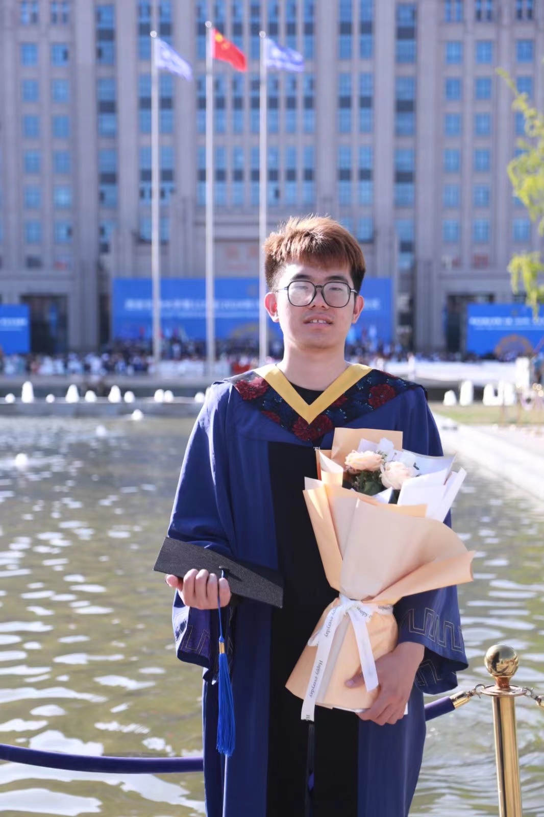 A person in a graduation gown holding flowersDescription automatically generated